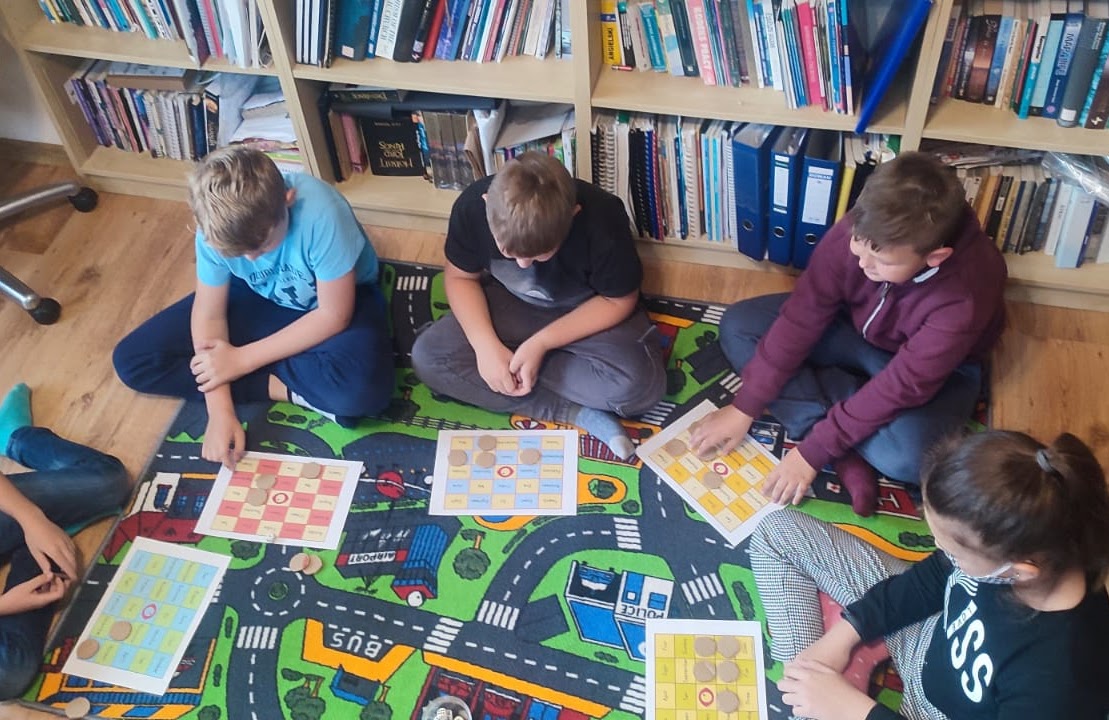 Older students play an English language board game on the classroom floor at Open Doors